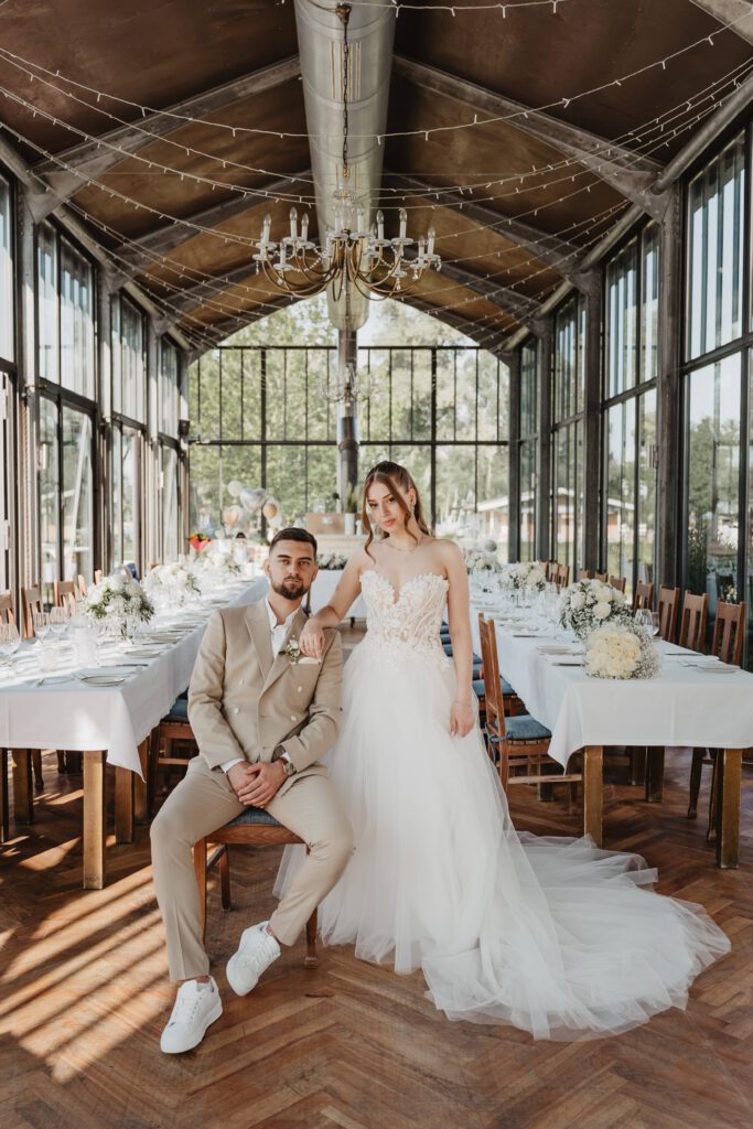 Bräutigam sitzt und die Braut steht daneben cool im schön dokorierten Sallers Badehaus Hochzeitsfotografin München Krystal Rey Photo